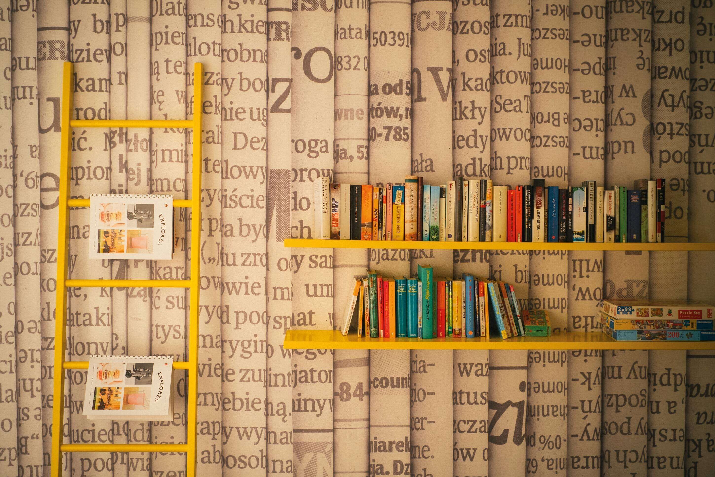 Een boekenplank met boeken en een gele ladder voor een muur met tekst.