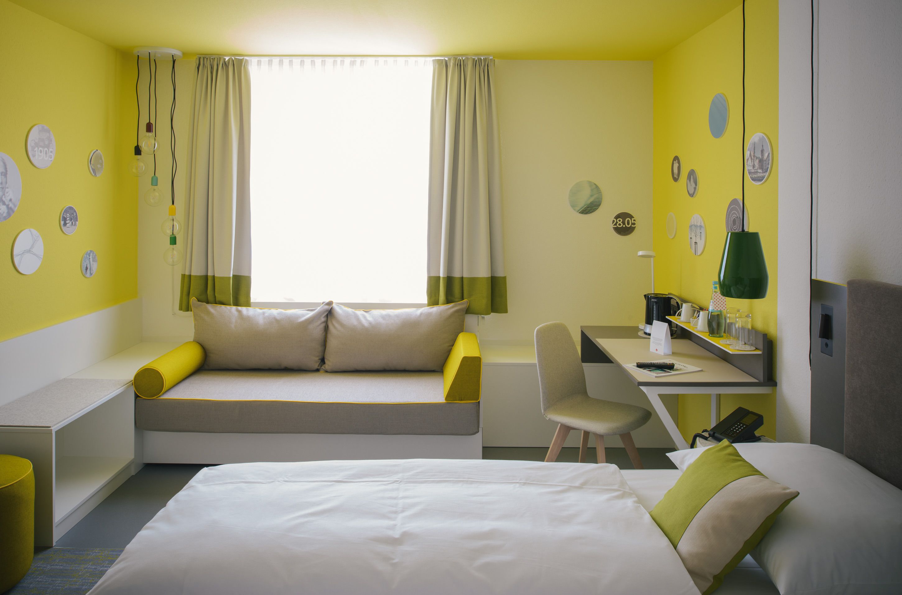 Habitación de hotel con cama, escritorio y silla. Cortinas en la ventana y paredes decoradas con platos redondos.