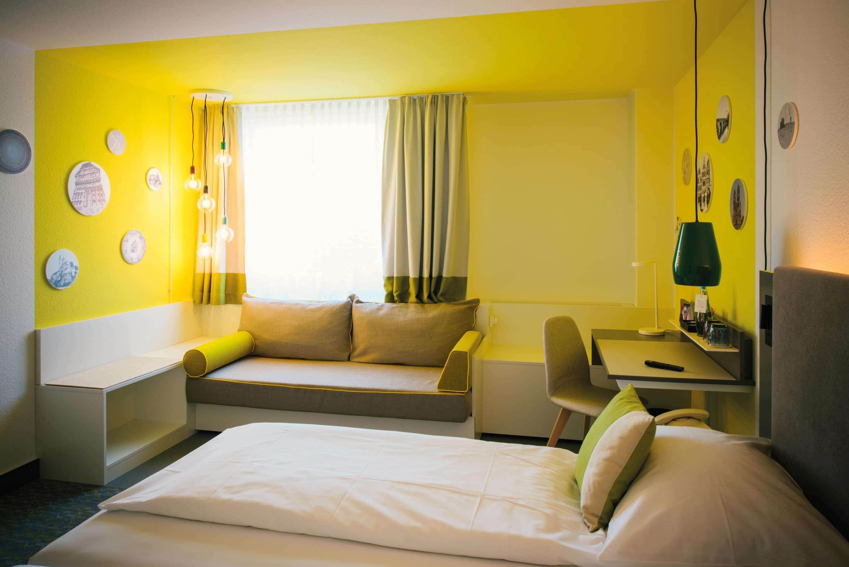 A hotel room with a bed, a desk, a chair, a sofa, and a window with curtains.