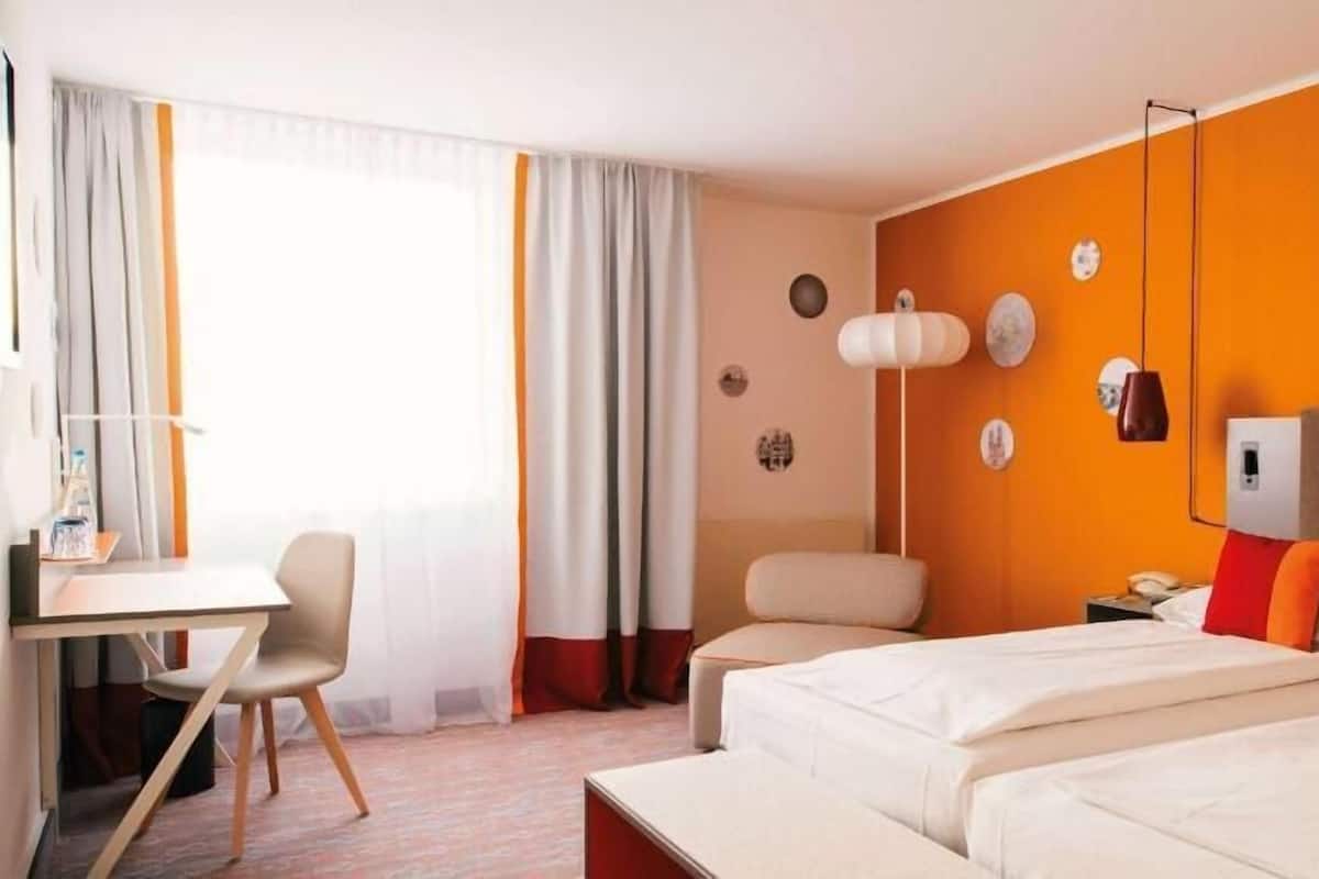 Une chambre d’hôtel avec deux lits, un bureau, une chaise et une fenêtre avec des rideaux.