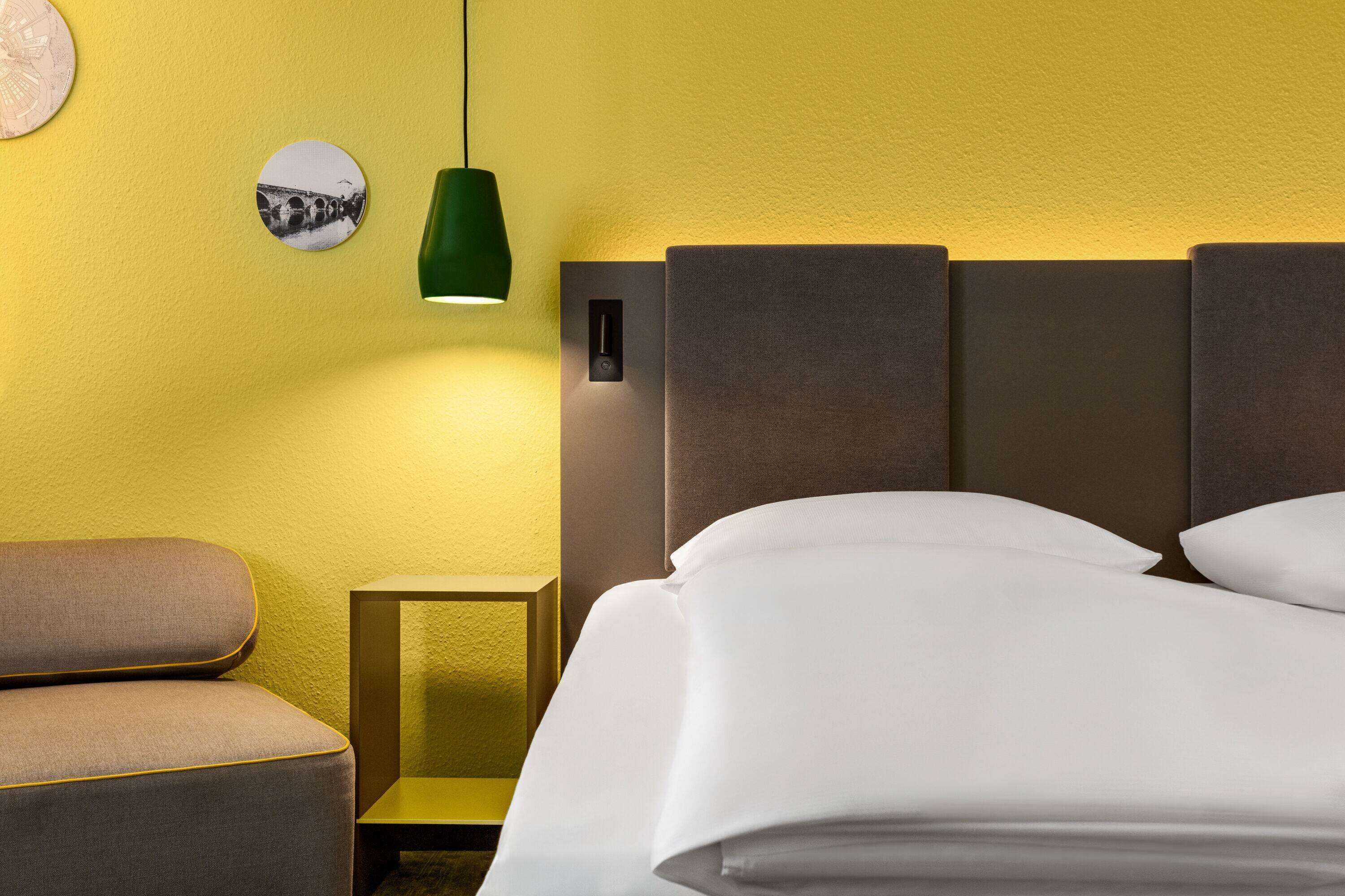 A hotel room with a bed, a nightstand, a lamp, and a wall-mounted picture.