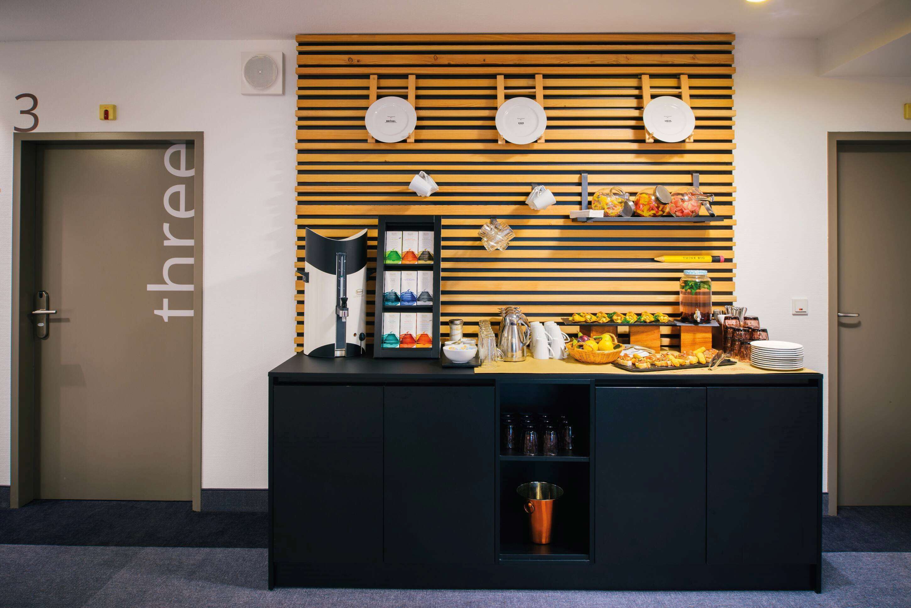 Un espace d’accueil avec un comptoir où sont exposés des aliments et des boissons, un porte-assiettes fixé au mur et un panneau indiquant le numéro de la salle.