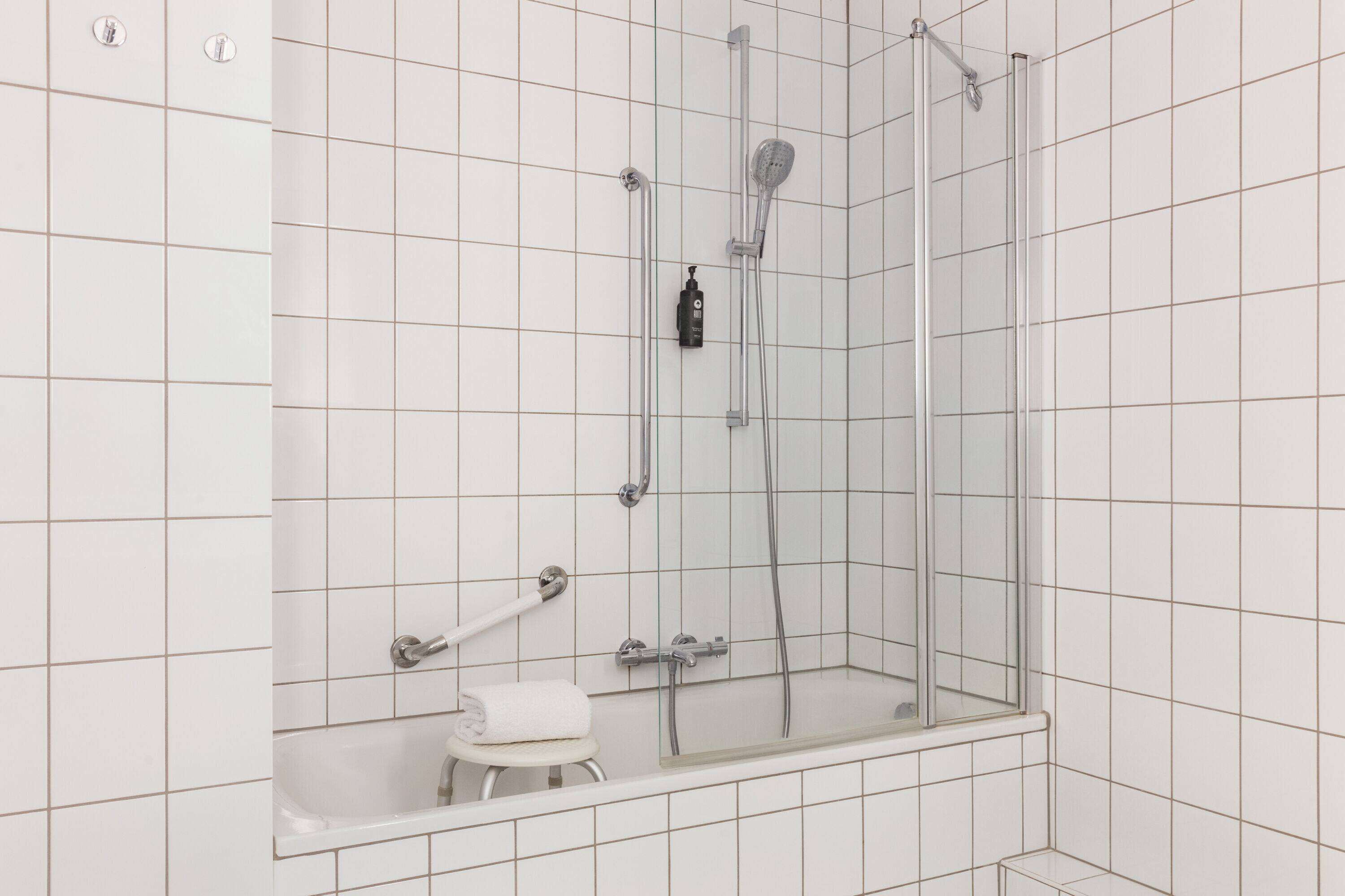 A modern bathroom with a glass-enclosed shower, a white bathtub, and a small stool with a towel.