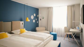 A hotel room with two beds, a desk, a chair, a lamp, and a large window with curtains.