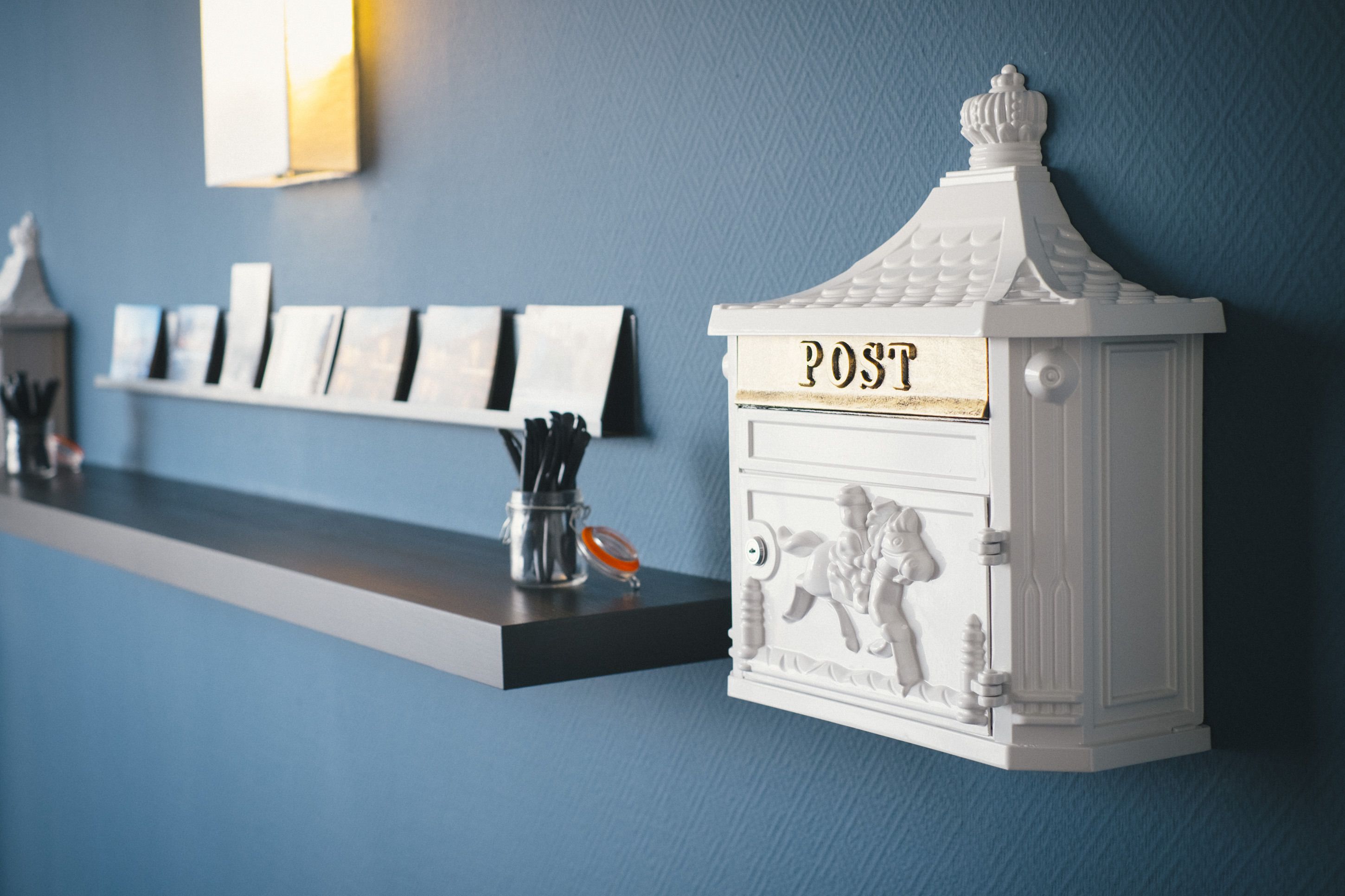 Een wandplank met ansichtkaarten en een decoratieve brievenbus met het opschrift 'POST'.