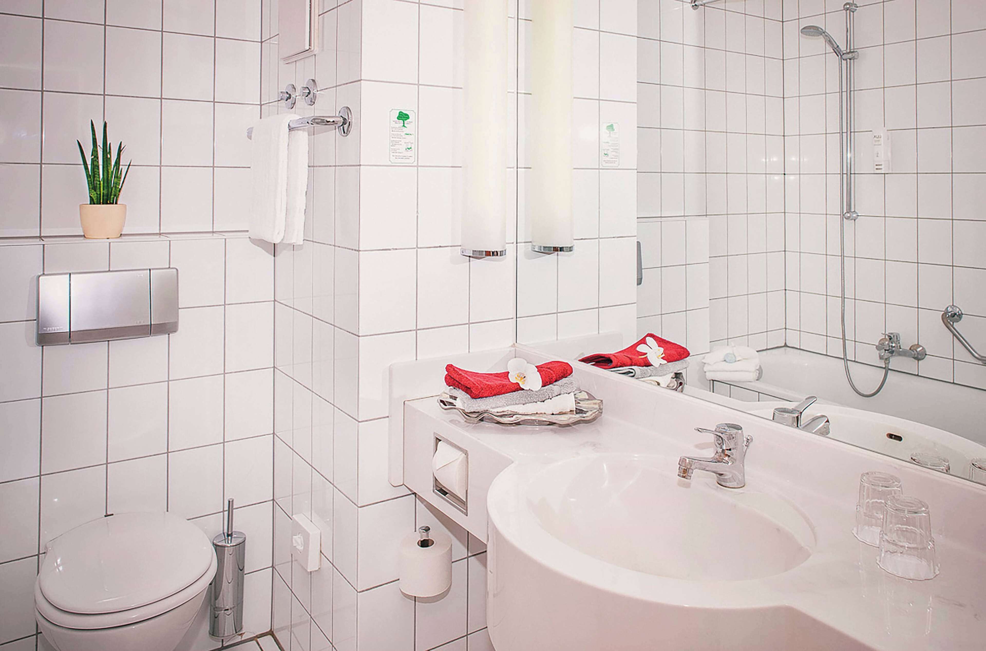 A modern bathroom with a toilet, sink, and shower. There is a potted plant on the wall, a towel rack, and a mirror above the sink.