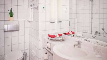 A modern bathroom with a toilet, sink, and shower. There is a potted plant on the wall, a towel rack, and a mirror above the sink.