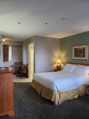 Habitación de hotel con cama, escritorio, silla, lámpara y un cuadro en la pared.