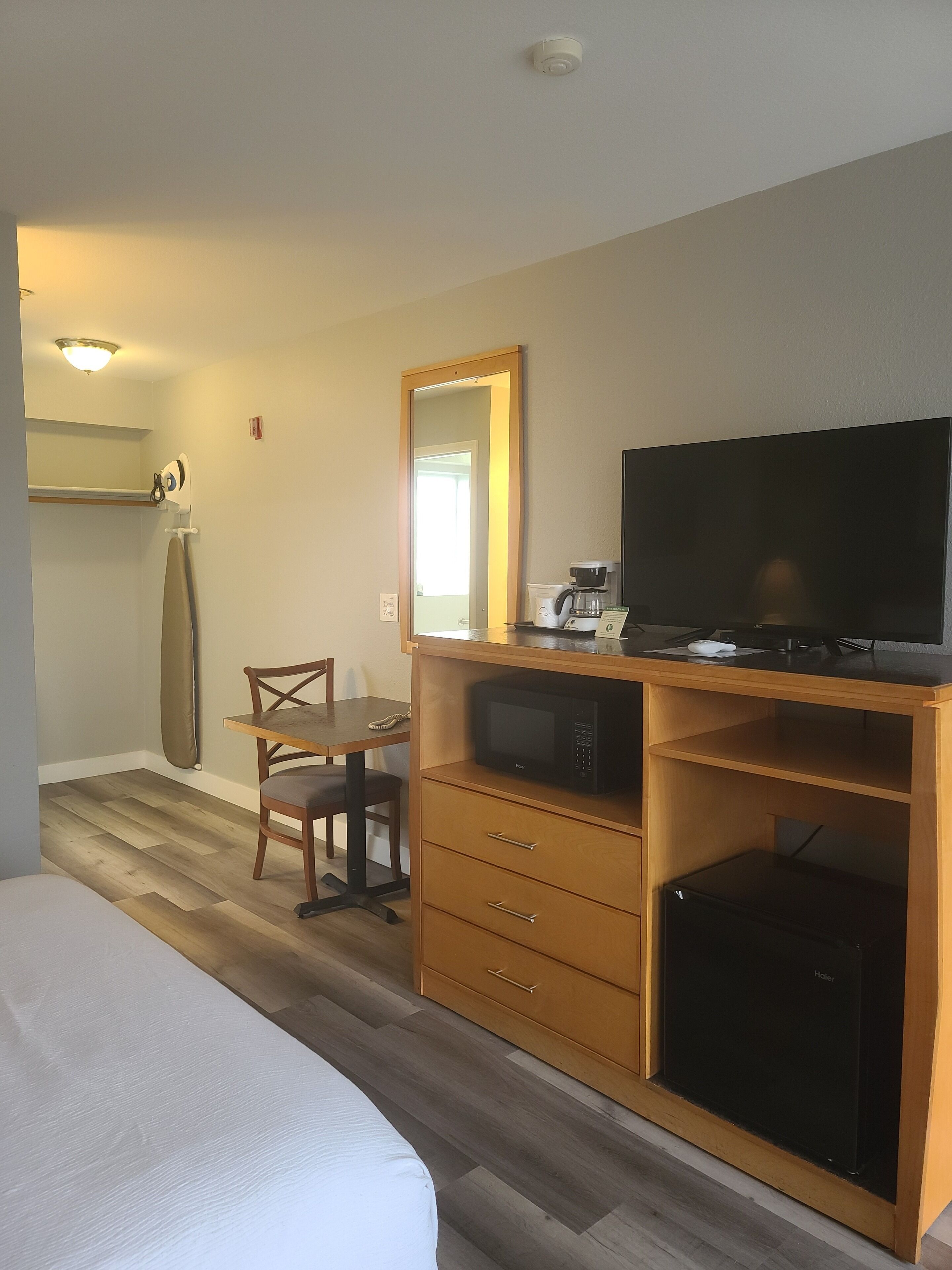 Habitación de hotel con cama, un escritorio de madera con televisor, microondas y refrigerador pequeño.