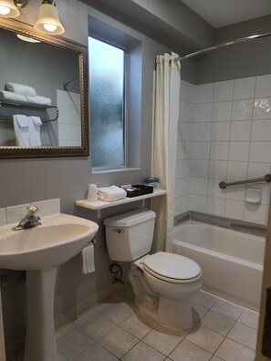 A bathroom with a sink, toilet, and bathtub. There is a window with a view of the outside, and a mirror above the sink.