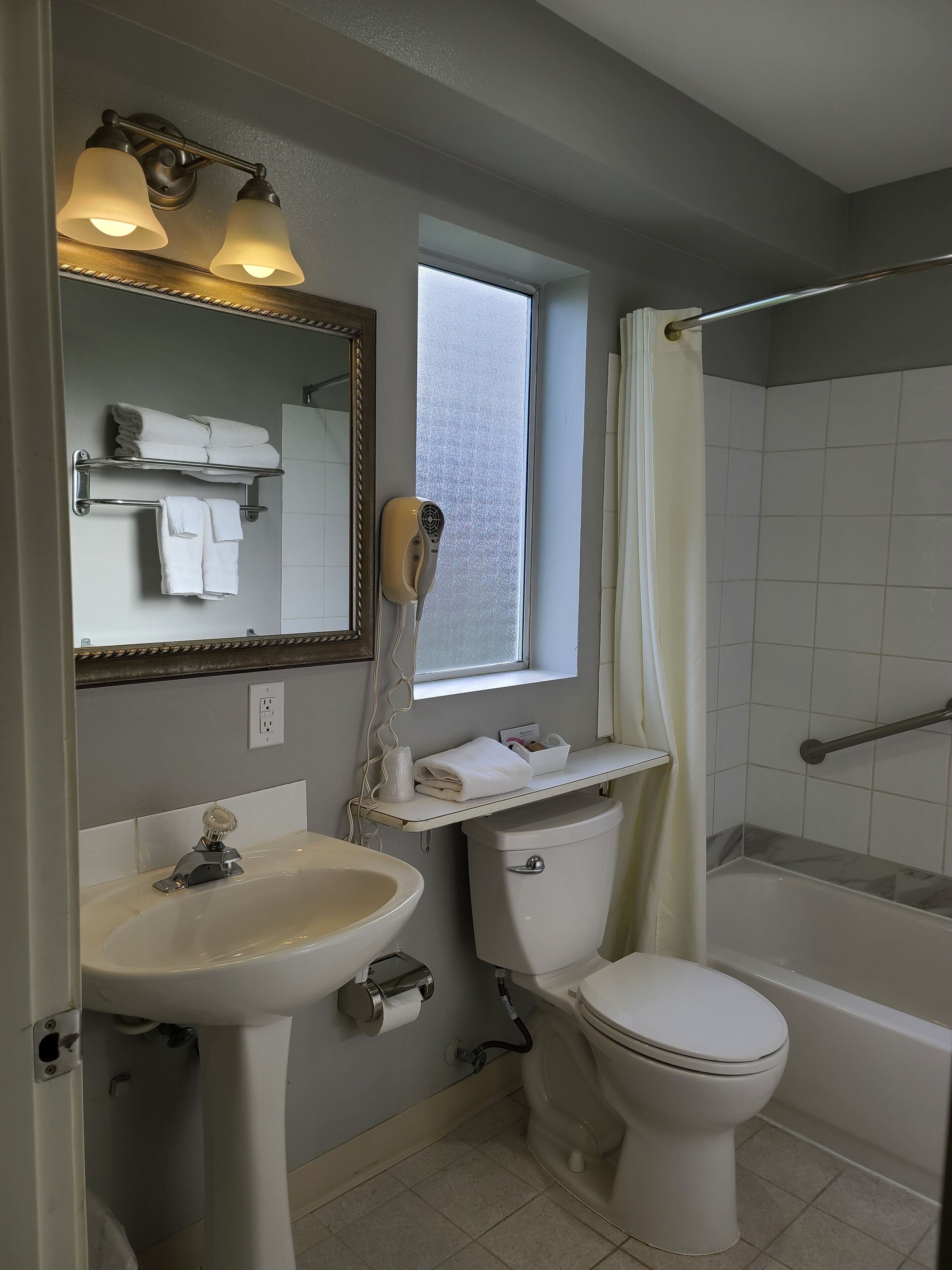 A bathroom with a sink, toilet, and bathtub. There is a window above the toilet and a towel rack with towels.