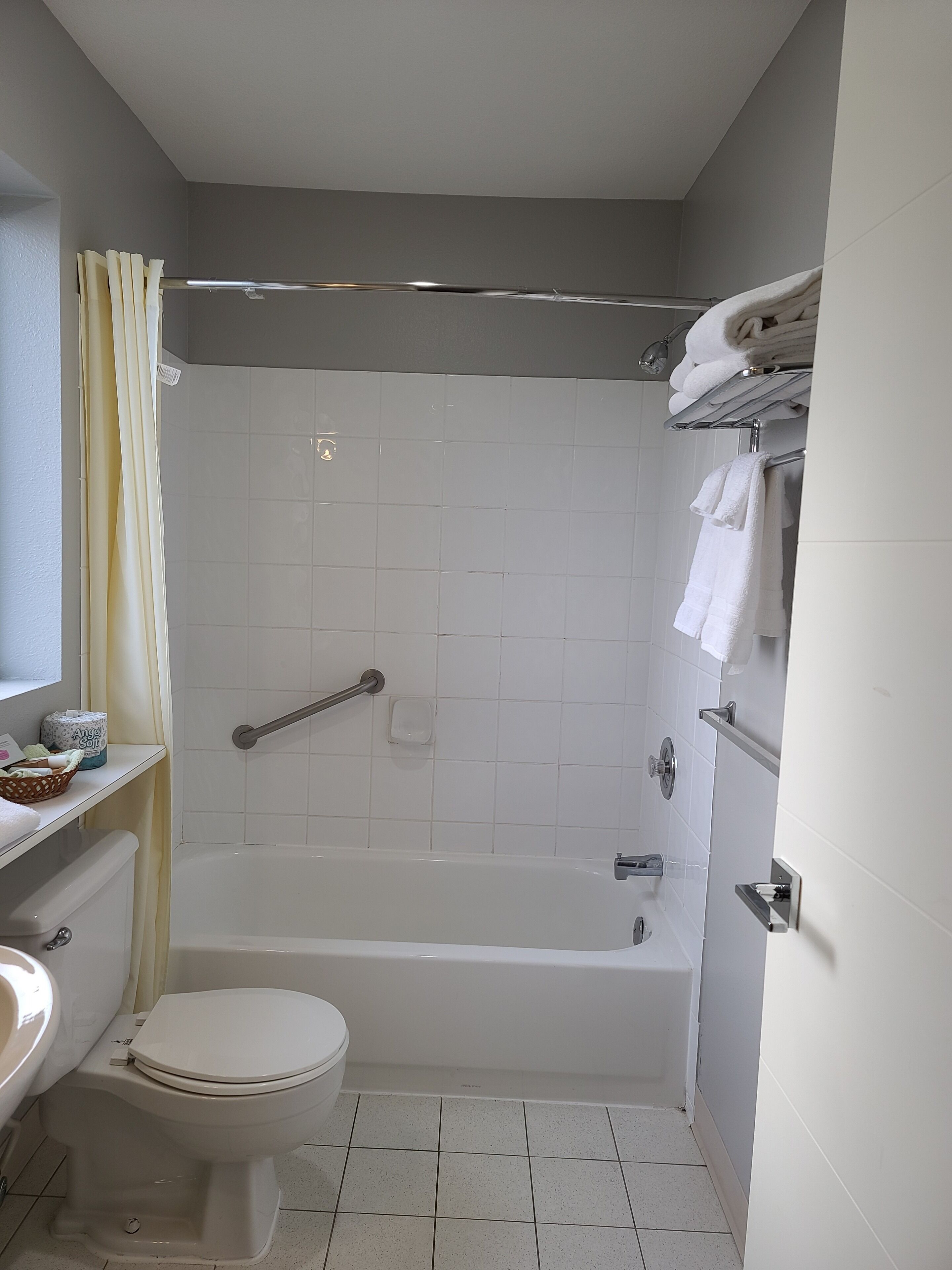 A bathroom with a bathtub, toilet, and sink. There is a shower curtain, a towel rack, and a soap dish.