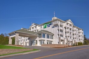 A multi-story hotel with a prominent green and white sign, featuring a modern architectural design with a flat roof and large windows.