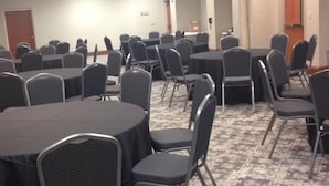 Une salle de conférence avec des tables et des chaises rondes, un revêtement de sol en moquette et une porte au fond.