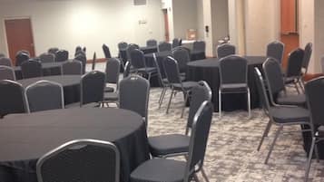 Un salón de conferencias con mesas y sillas redondas, suelo alfombrado y una puerta al fondo.