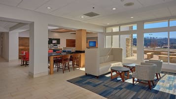 A modern hotel lobby with a bar area, seating, and large windows offering a view of the outdoors.