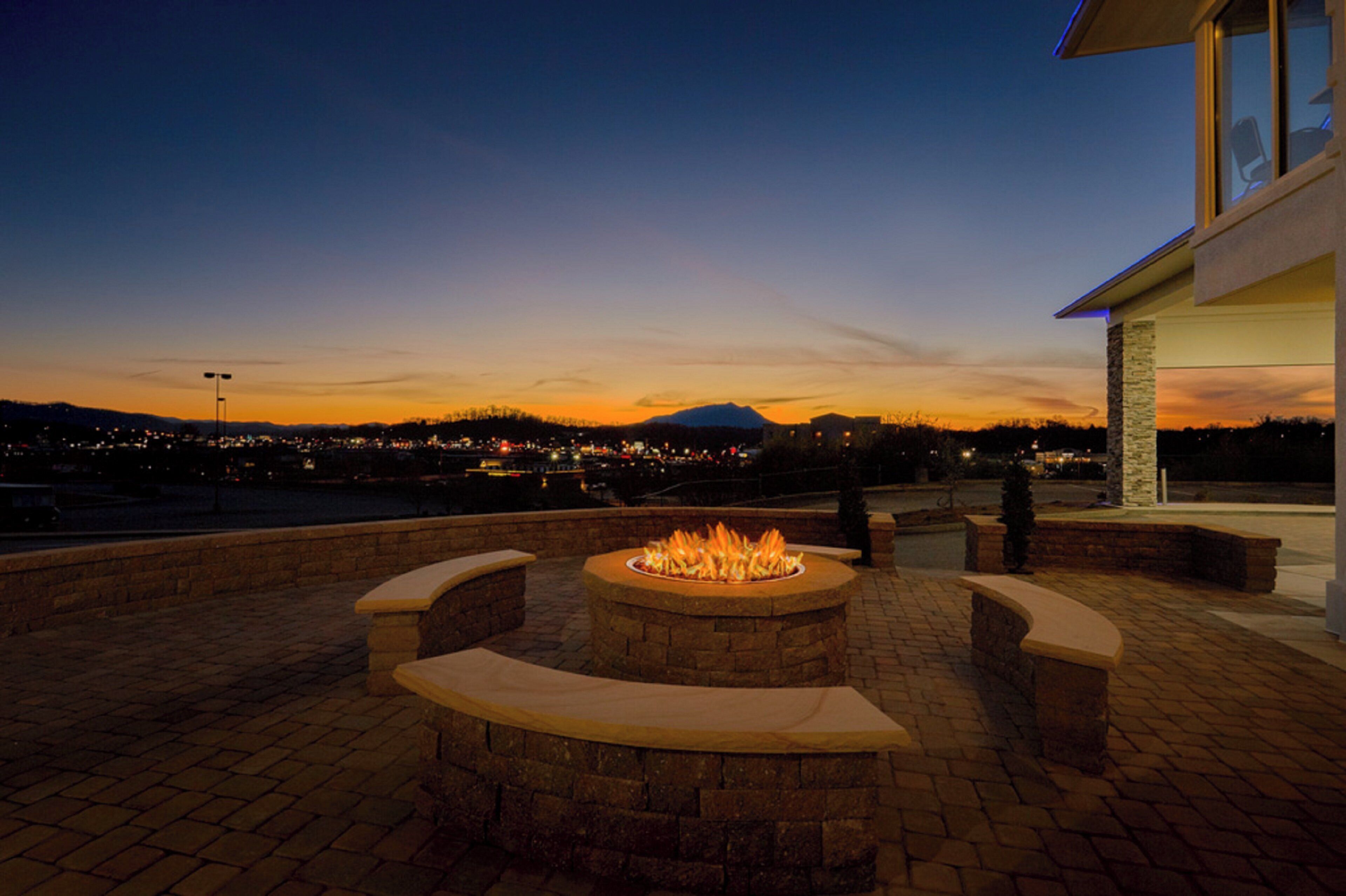 An outdoor fire pit area with a view of a cityscape at dusk.