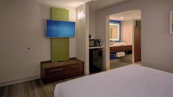 A hotel room with a bed, a TV, a minibar, a desk, and a bathroom visible through an open door.