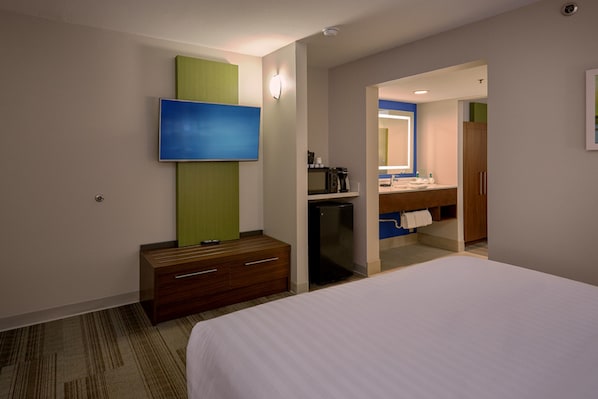 A hotel room with a bed, a TV mounted on the wall, a small desk with drawers, and a bathroom visible through an open door. - Holiday Inn Express and Suites Pigeon Forge Sevierville by IHG (Sevierville)