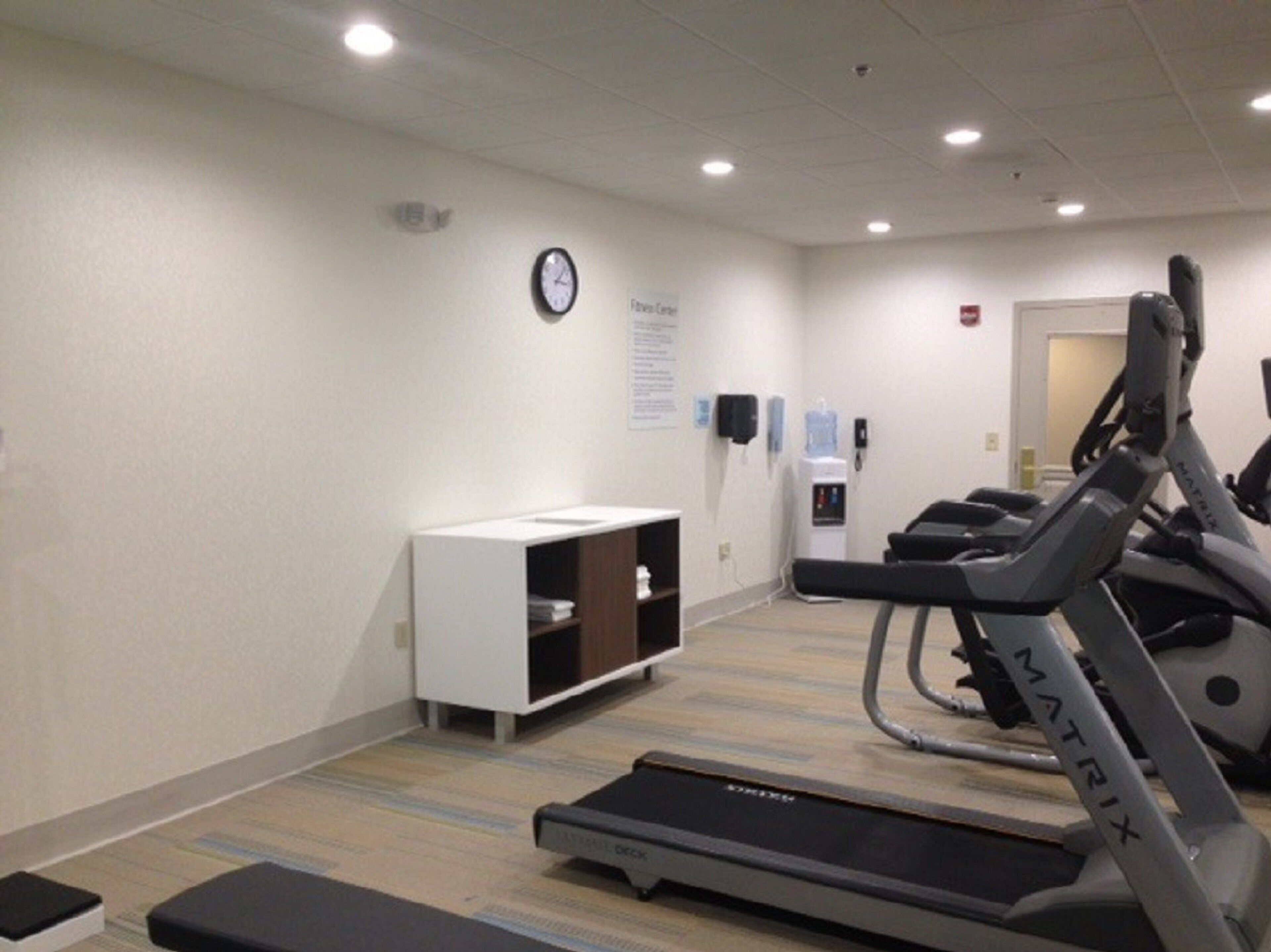 A fitness room with treadmills, a water dispenser, and a clock on the wall.