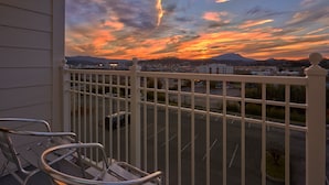 Un balcon donnant sur un parking et sur des montagnes lointaines, au coucher du soleil.