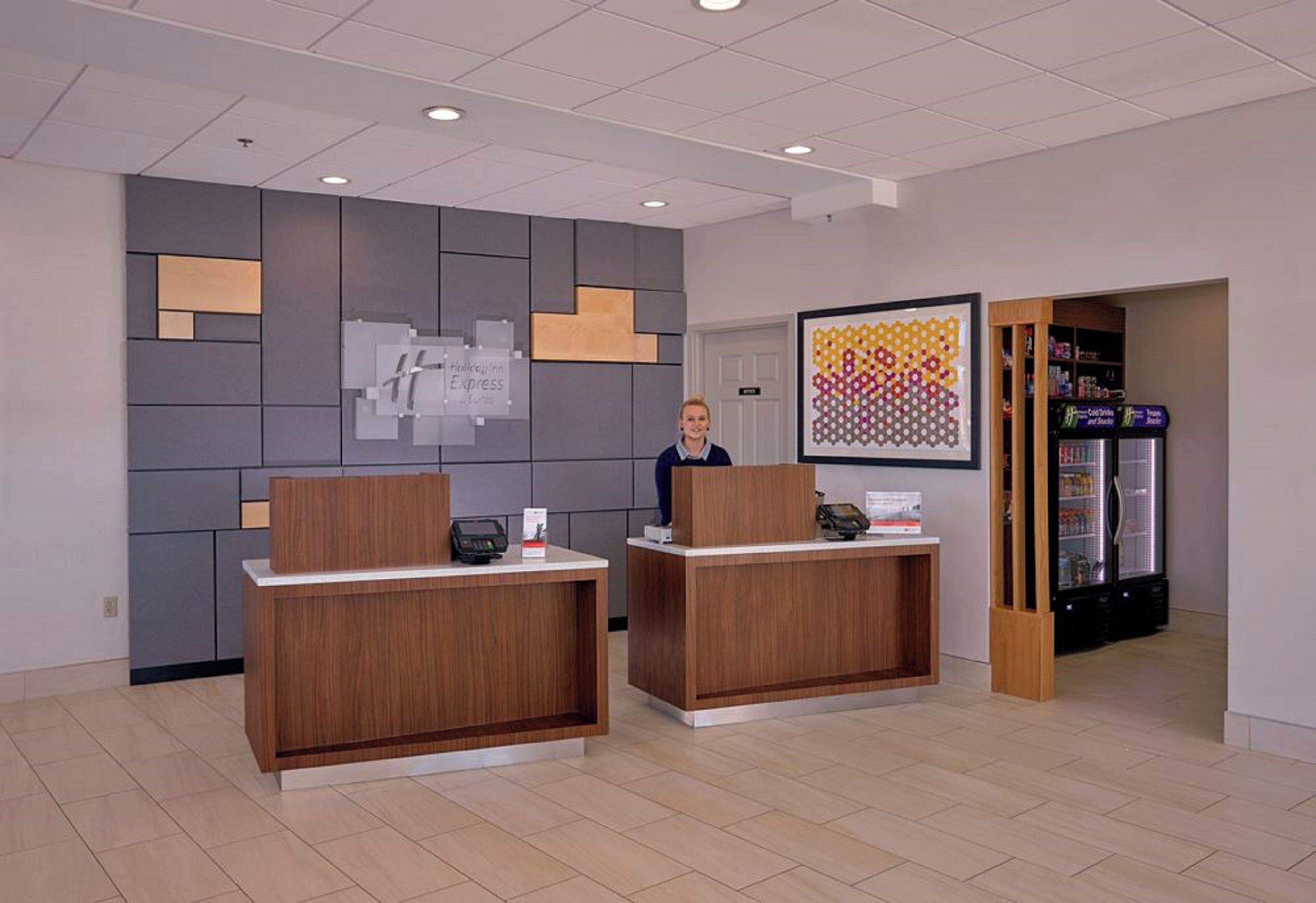 A reception area with two wooden reception desks, a digital kiosk, and a refrigerator stocked with beverages.