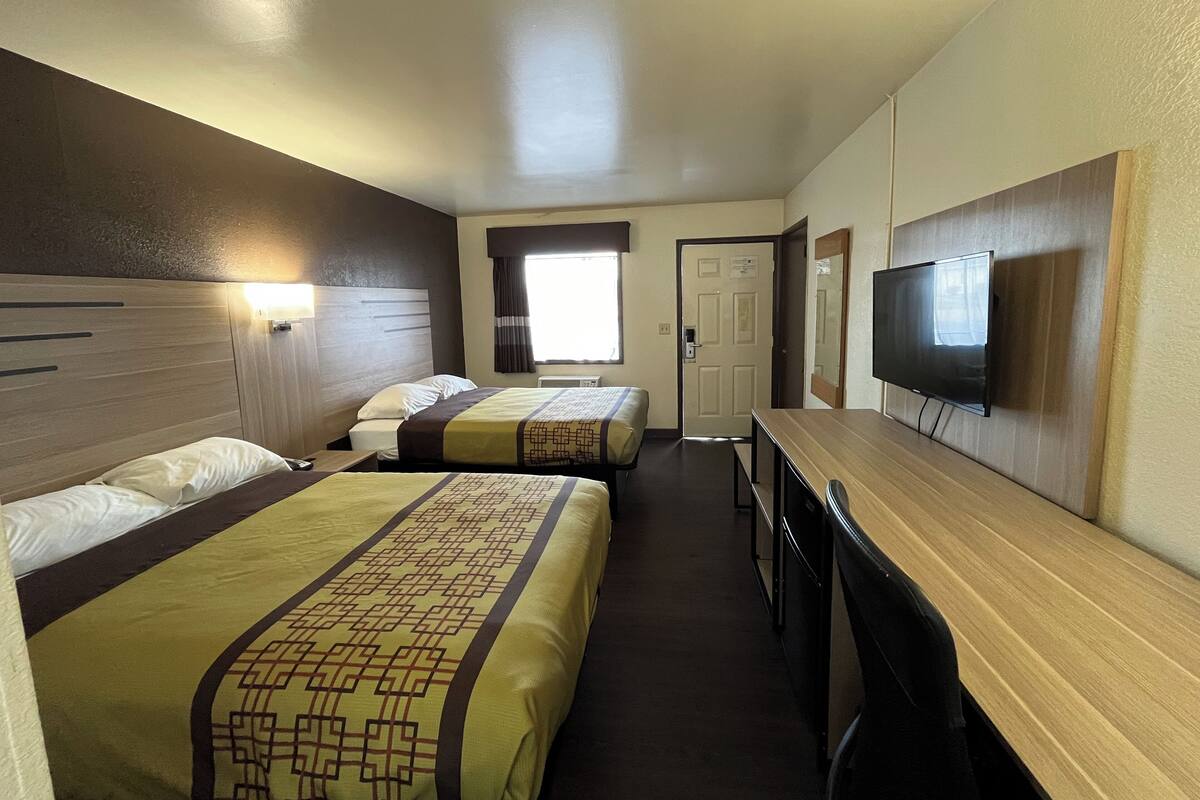 A hotel room with two beds, a TV, a desk, and a window.