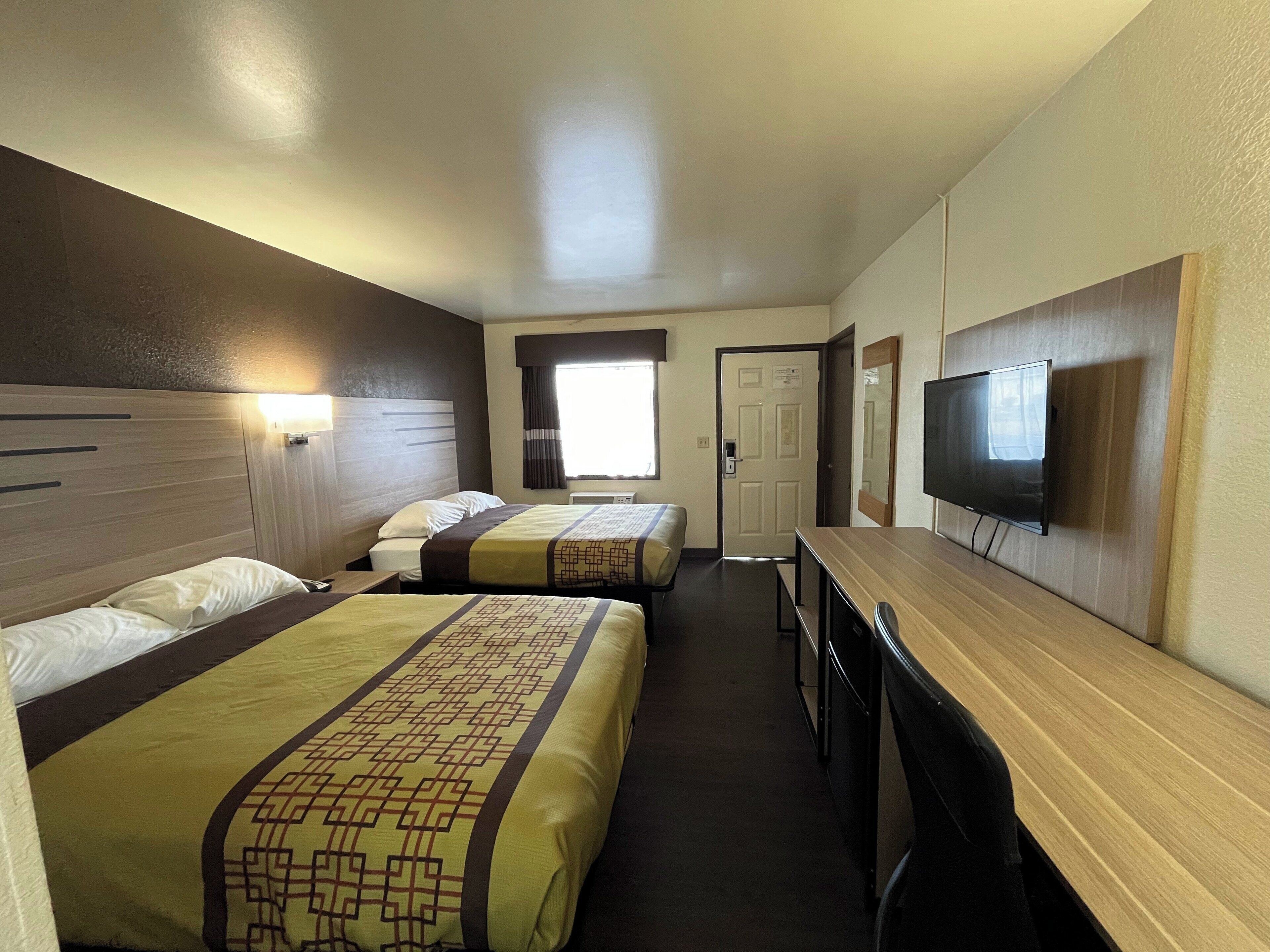 A hotel room with two beds, a TV, a desk, and a door leading to another room.