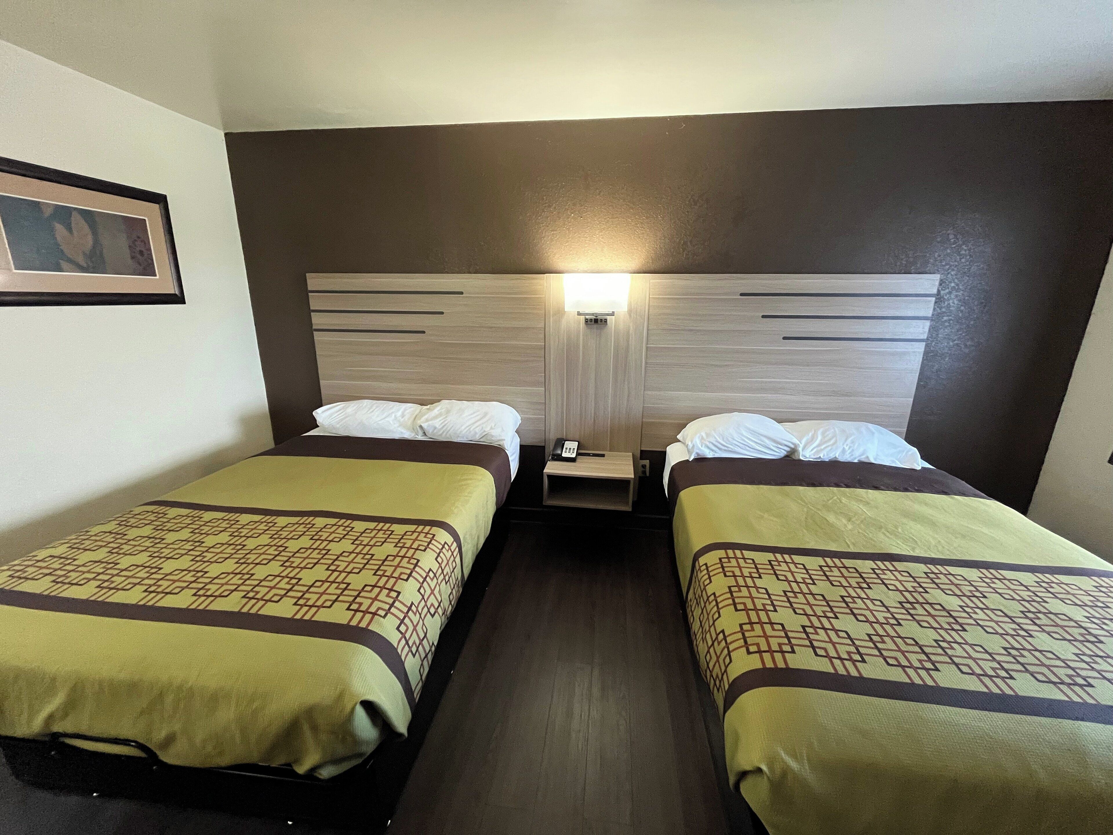 A hotel room with two beds, a nightstand with a phone, and a wall-mounted light.