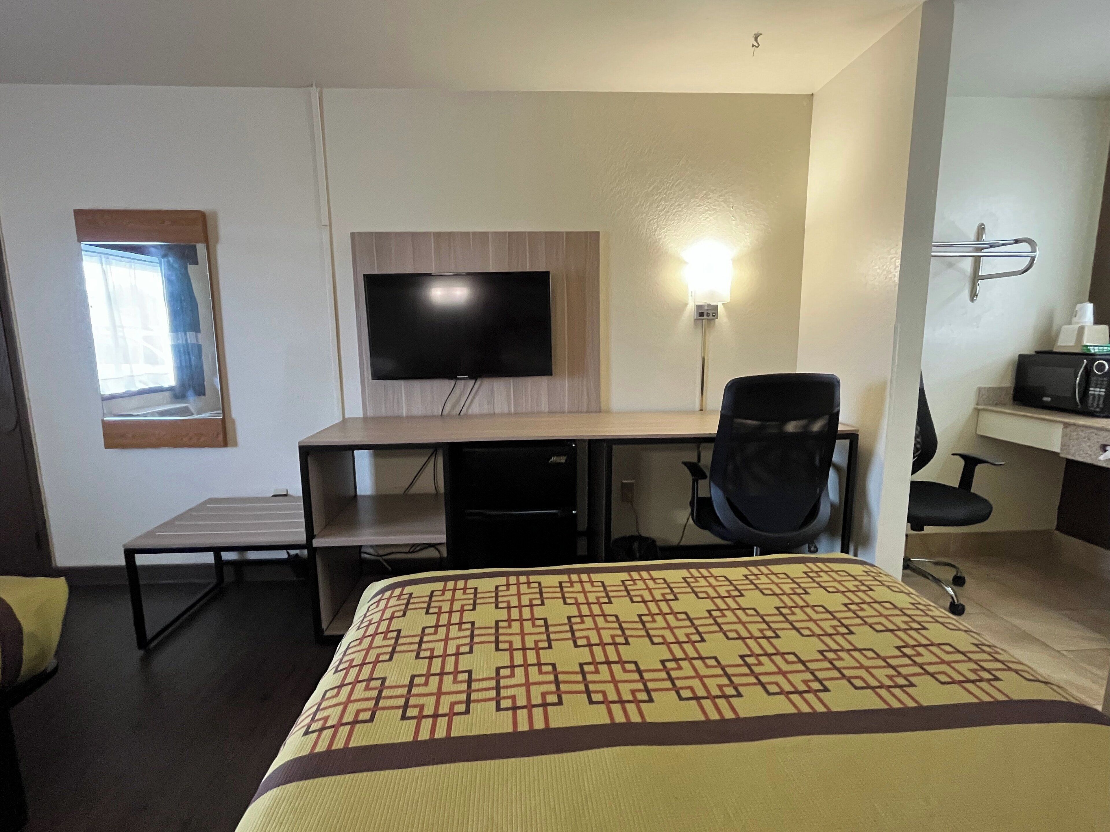 Habitación de hotel con cama, escritorio, silla, televisor, microondas y ventana pequeña.