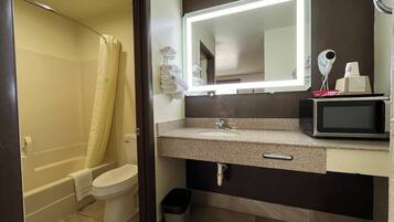 Un bagno con il water, un lavandino, uno specchio e un forno a microonde sul ripiano.