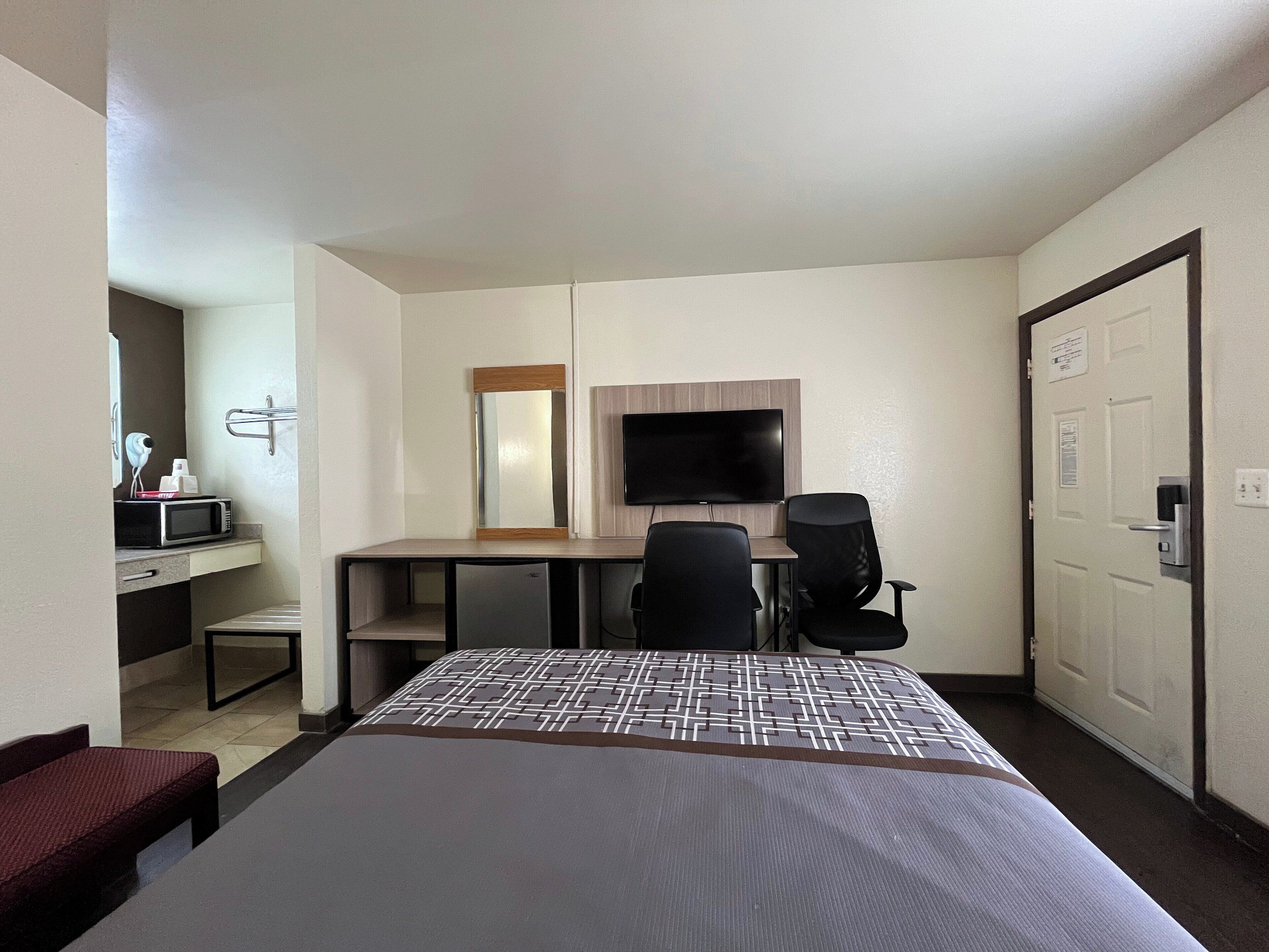 Una habitación de hotel con cama, escritorio con silla, televisión, microondas y puerta.