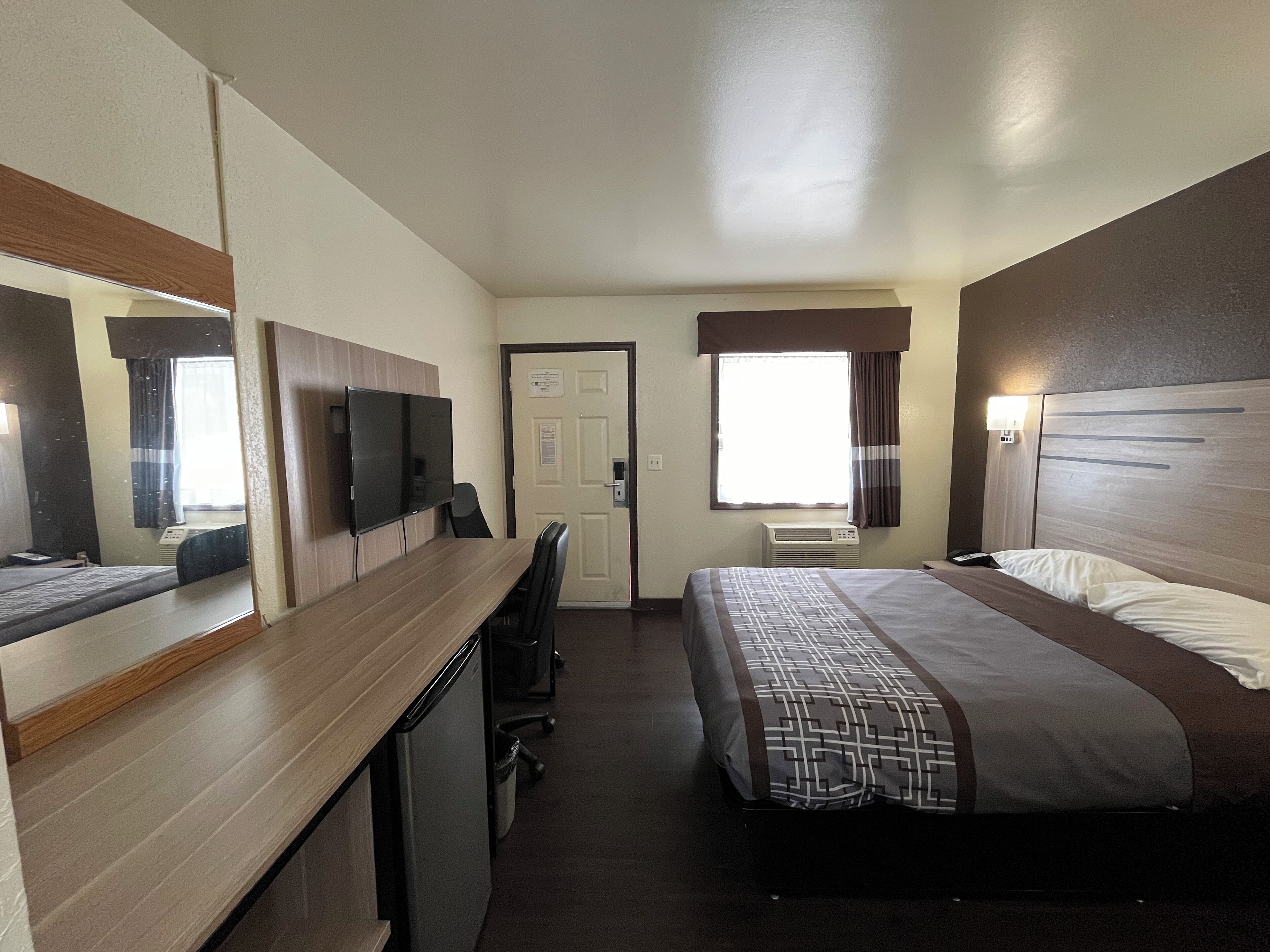 Ein Hotelzimmer mit Bett, Schreibtisch, Fernseher, Tür und einem blickdichten Fenster.