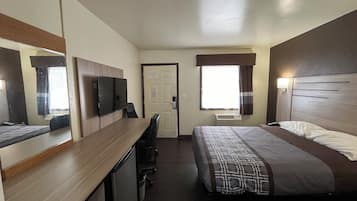 Ein Hotelzimmer mit Bett, Schreibtisch, Fernseher, Tür und einem blickdichten Fenster.