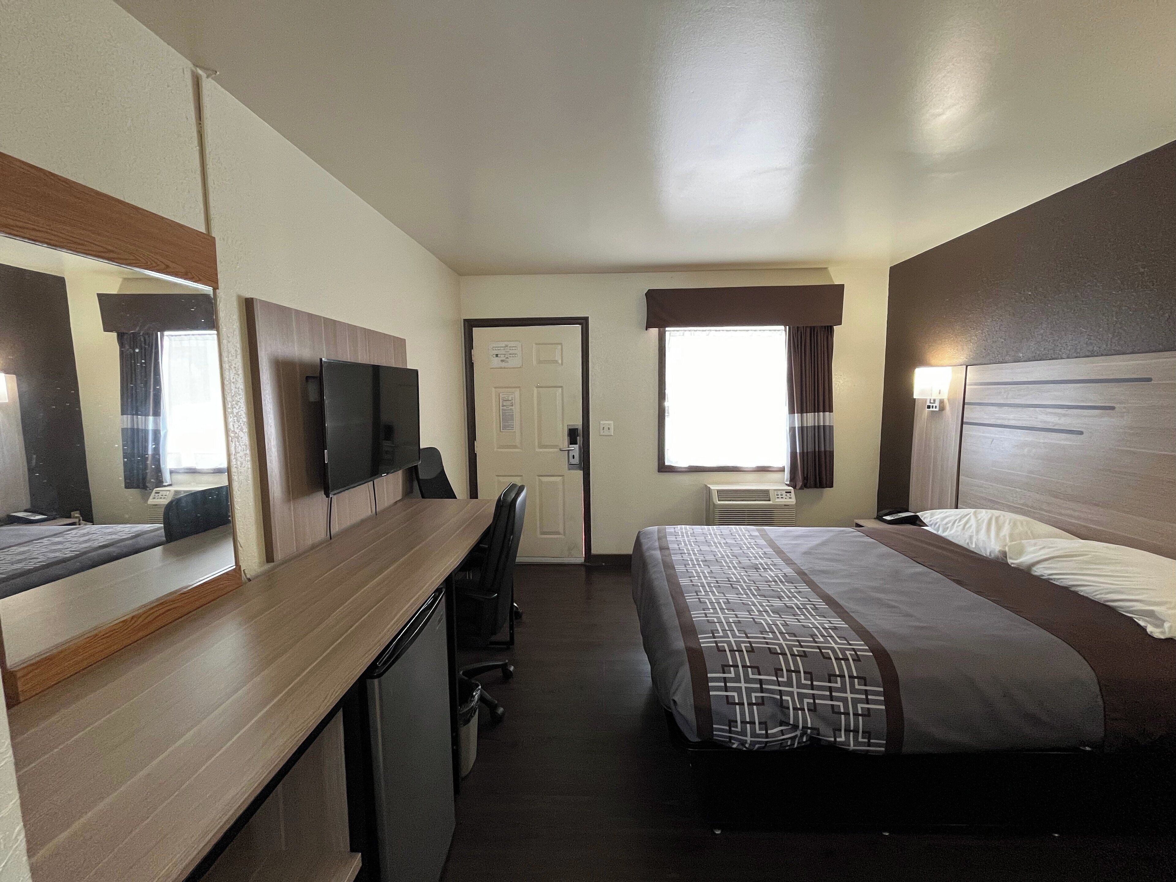 Une chambre d’hôtel équipée d’un lit, d’un bureau, d’une télévision, d’une fenêtre avec des rideaux et d’un appareil de climatisation.
