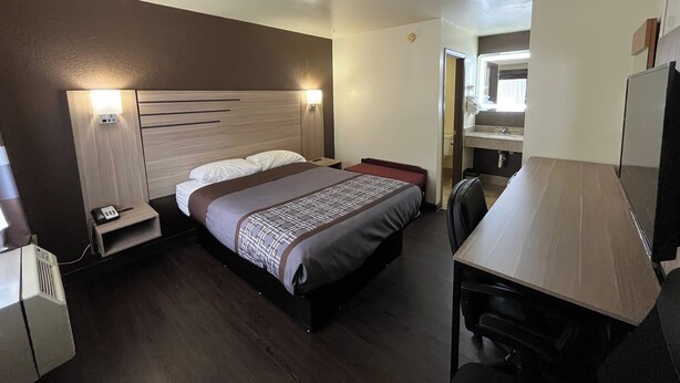 A hotel room with a bed, bedside table, desk, chair, and a mirror. - Budget Inn (Nassawadox)