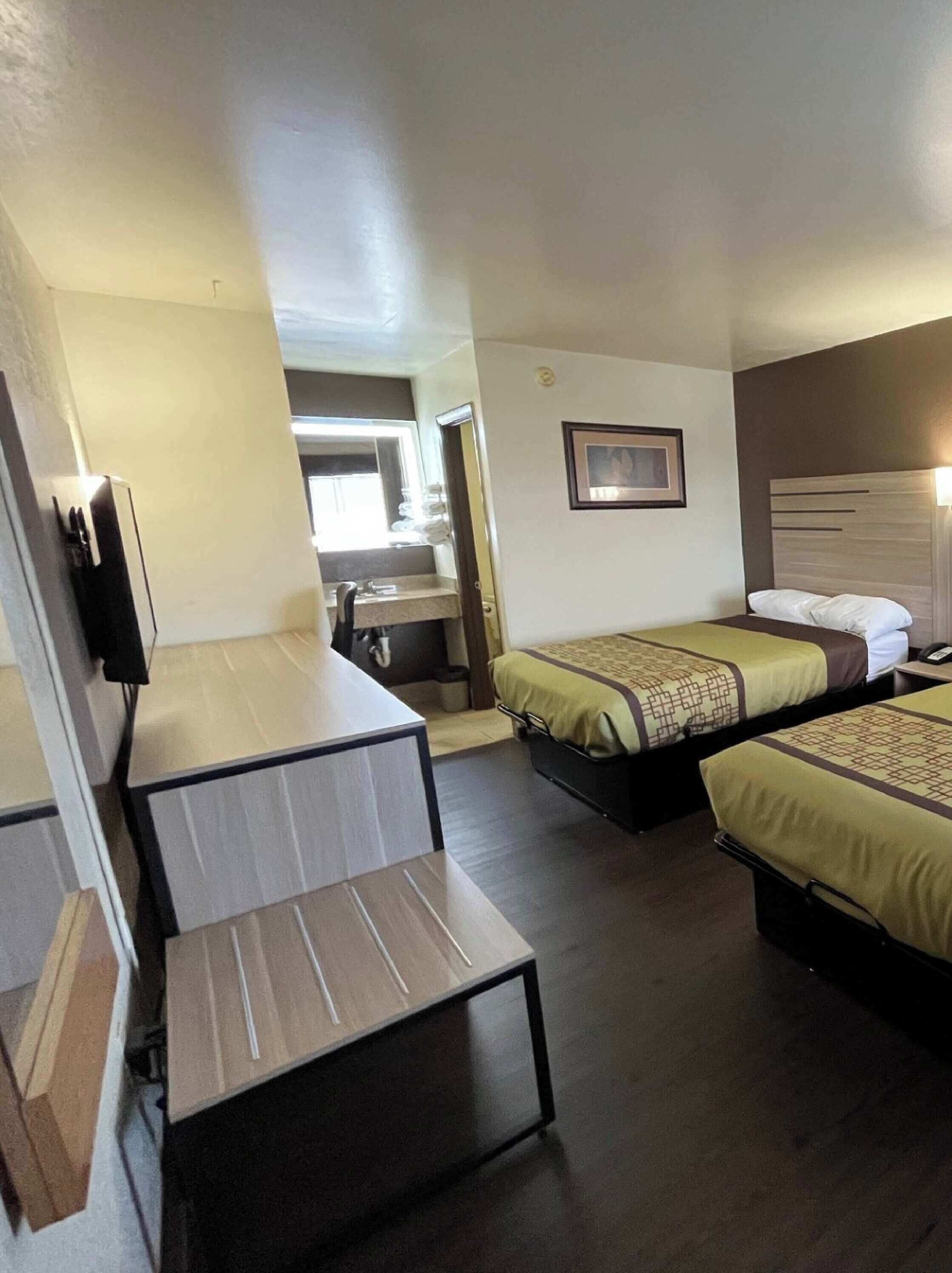 A hotel room with a desk, two beds, a TV, and a bathroom visible through an open door.