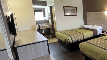 A hotel room with a desk, two beds, a TV, and a bathroom visible through an open door.