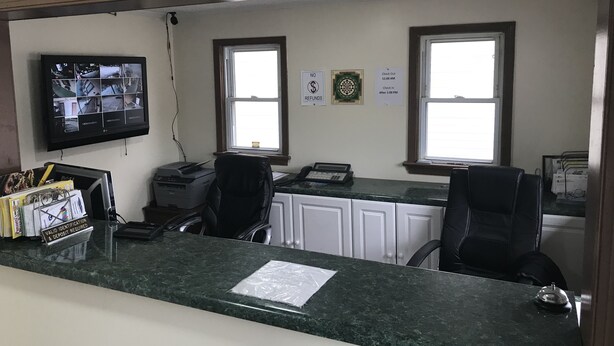 Zona de recepción con mostrador de mármol, dos sillas de oficina negras, una impresora y un monitor de seguridad.