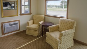 Una habitación de esquina con dos sillones estampados, una mesita, un espejo y una ventana con vista a un estacionamiento.