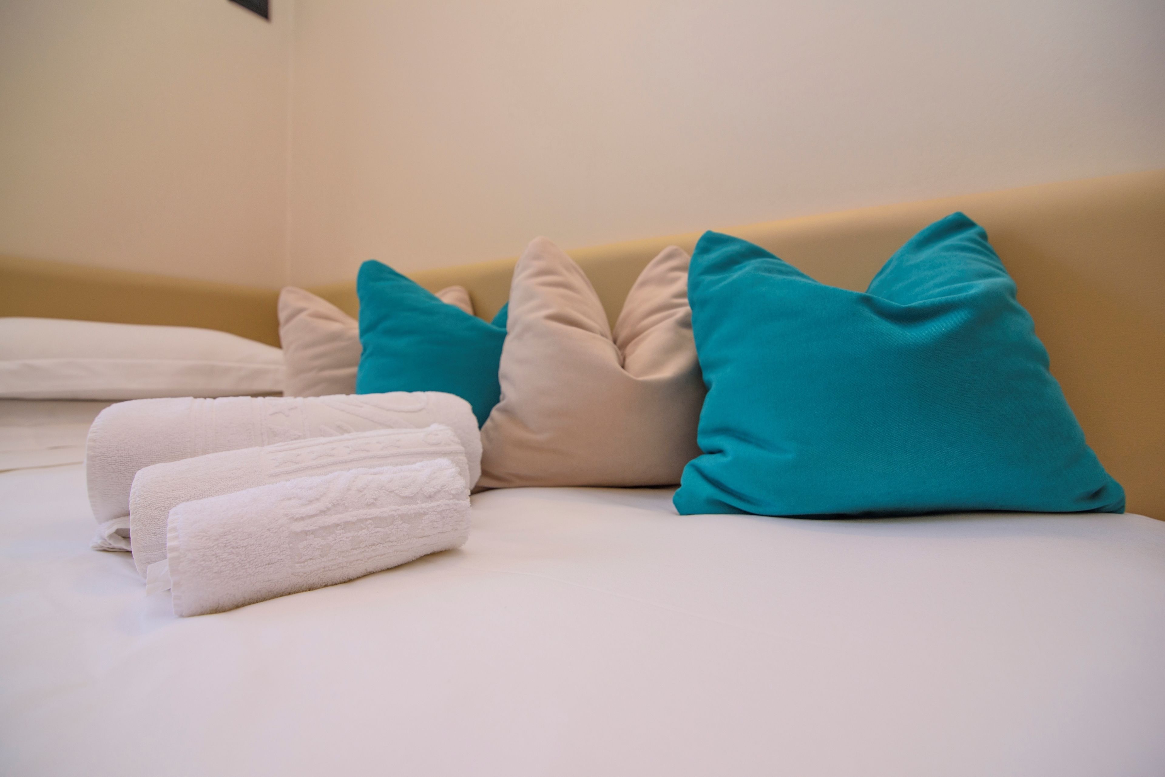 Een bed met witte en teal kussens, en twee witte handdoeken.
