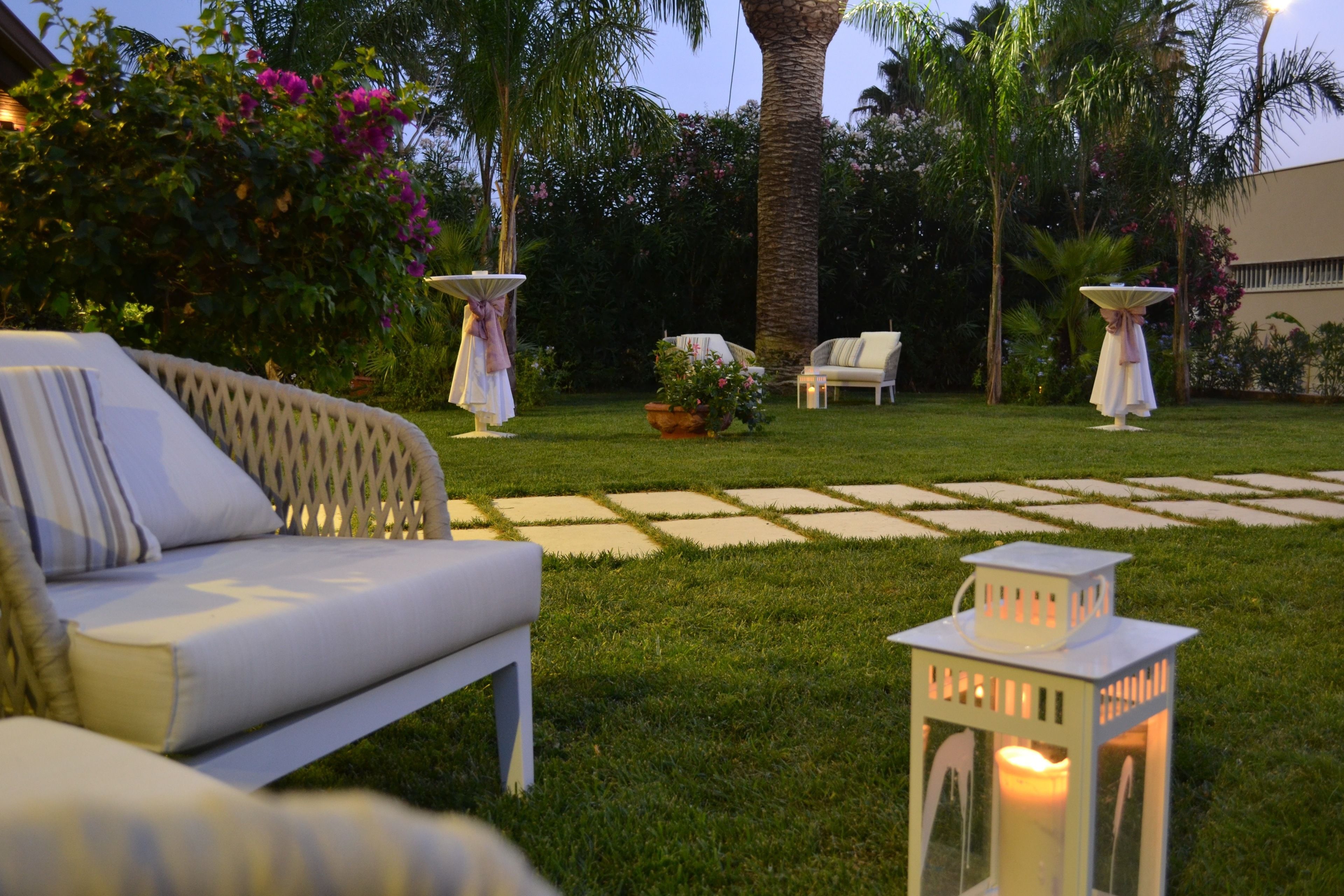 A garden patio with a white sofa, two white tables with umbrellas, and a lantern.
