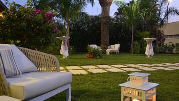 A garden patio with a white sofa, two white tables with umbrellas, and a lantern.