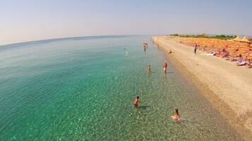 Une plage avec une eau turquoise et limpide où l’on peut se baigner. On y trouve des parasols et des chaises longues sur le sable.