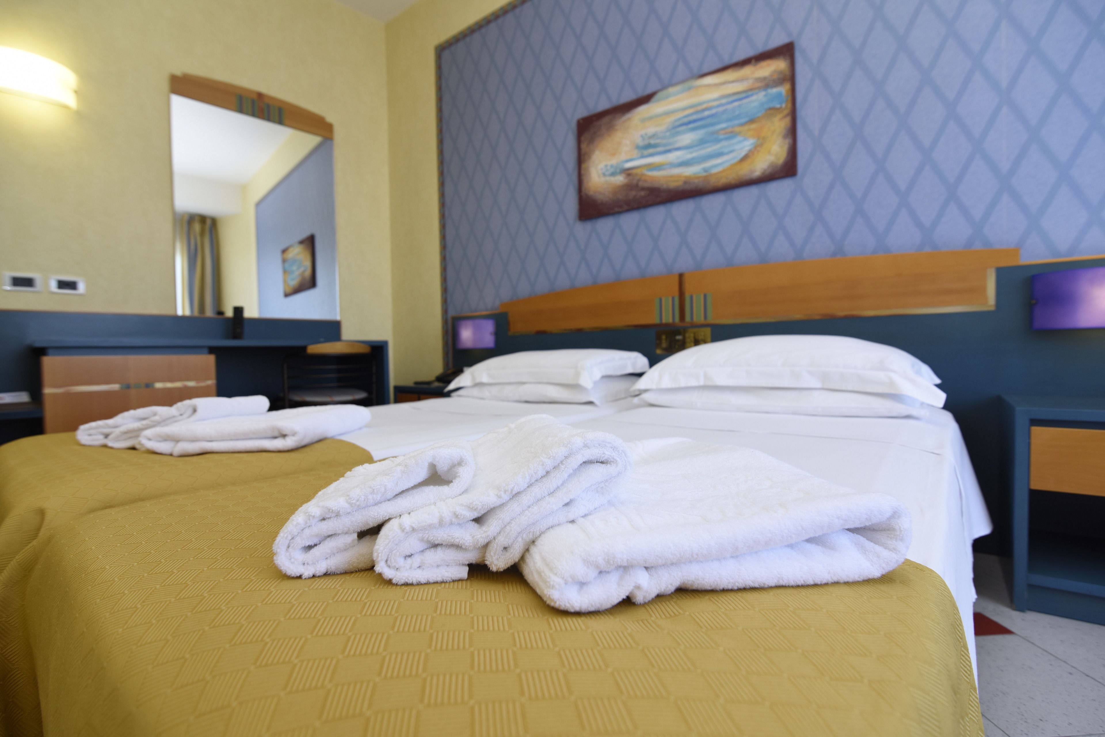 A hotel room with a bed, a desk, a mirror, and a painting on the wall.