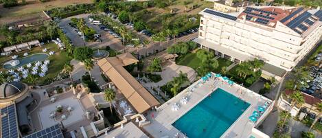 Vue aérienne d’un complexe hôtelier doté d’une grande piscine, de plusieurs espaces de restauration et d’un parking.
