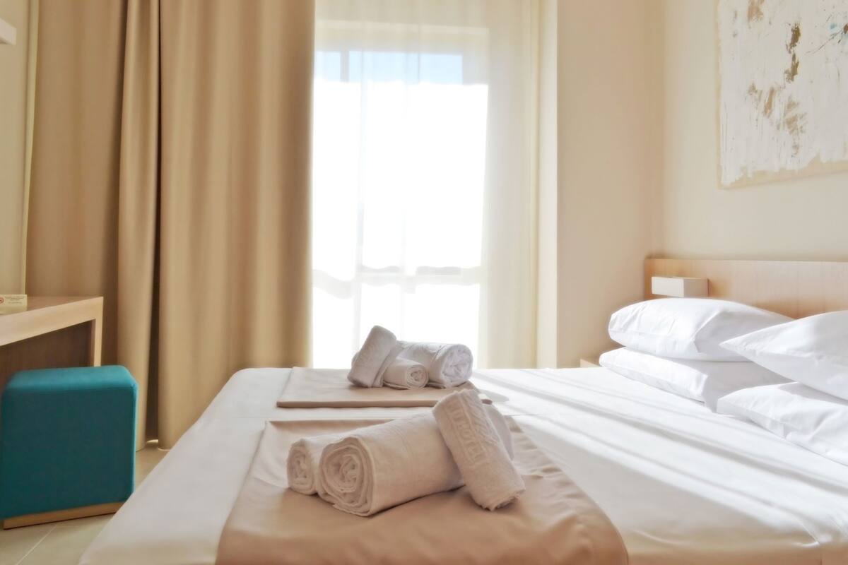 Ein Hotelzimmer mit Bett, Schreibtisch, Stuhl und einem fenster mit Vorhängen.