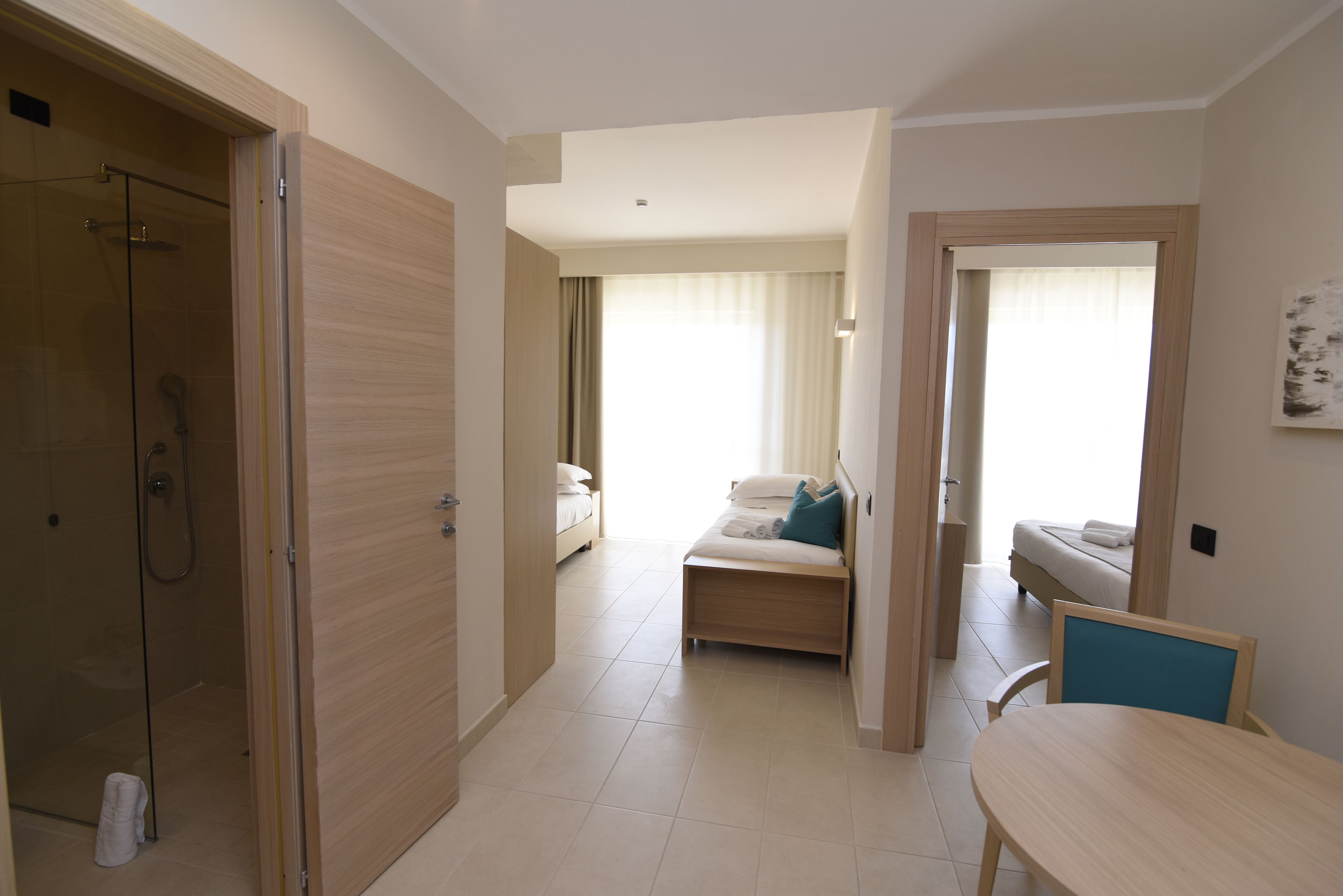 Habitación de hotel con ducha, cama, zona de estar con mesa y vistas al exterior.