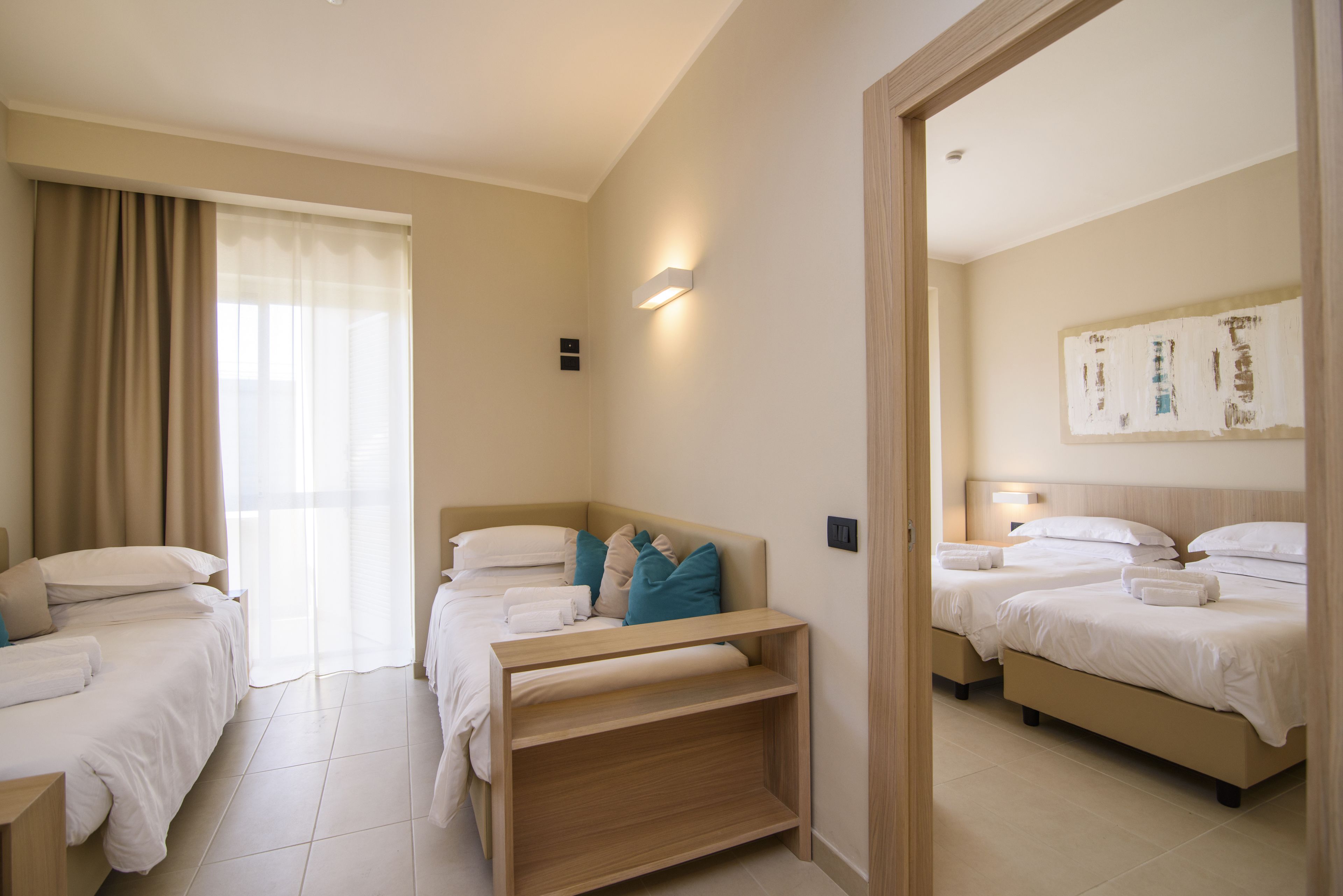 Une chambre d’hôtel avec deux lits simples, un banc en bois et une grande fenêtre avec des rideaux.