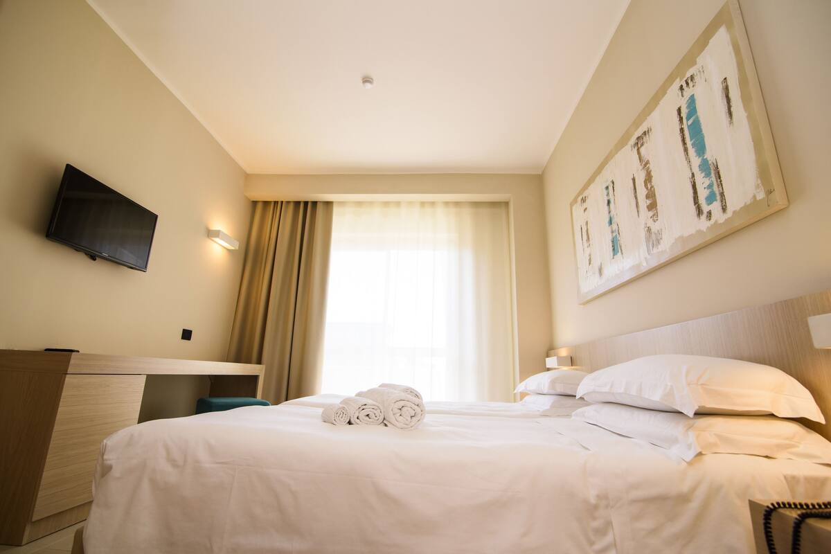 Ein Hotelzimmer mit Bett, Schreibtisch, Flachbildfernseher und einem Bild an der Wand.
